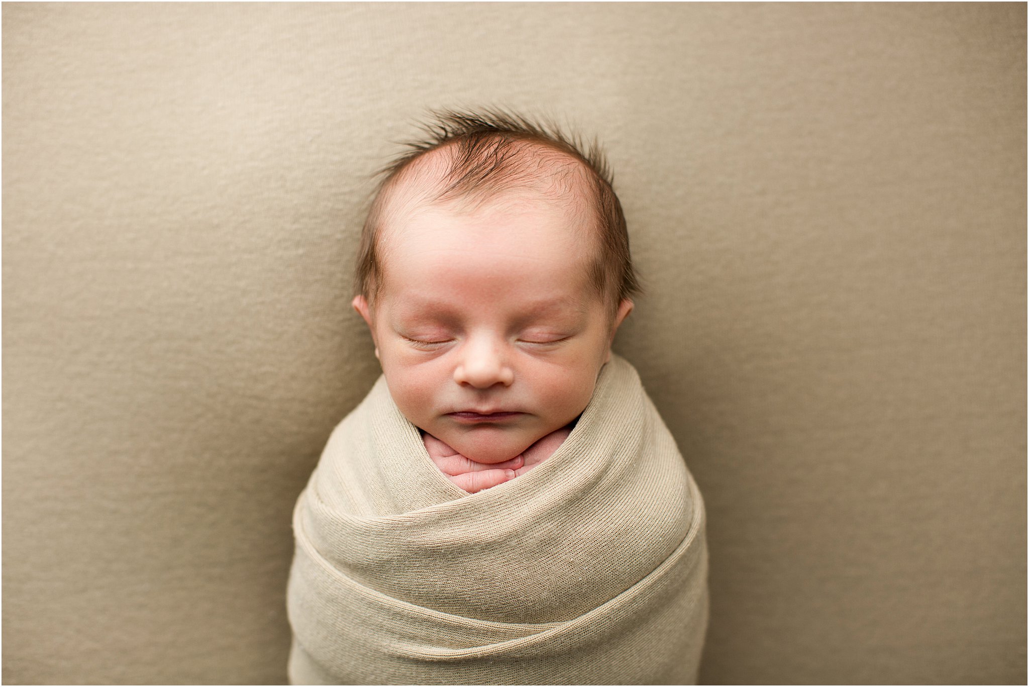 newborn baby boy wrapped in tan fabric sleeping