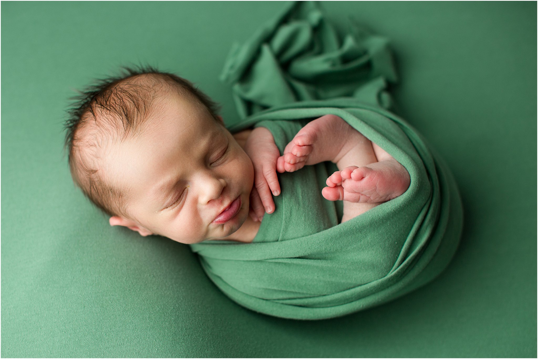 newborn boy pouty lip wrapped on green fabric