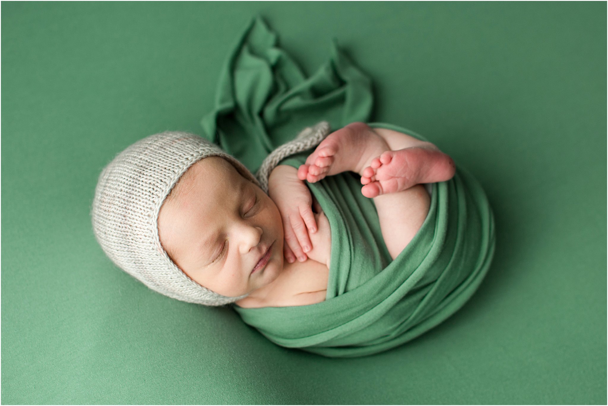 newborn boy in green wrap and bonnet