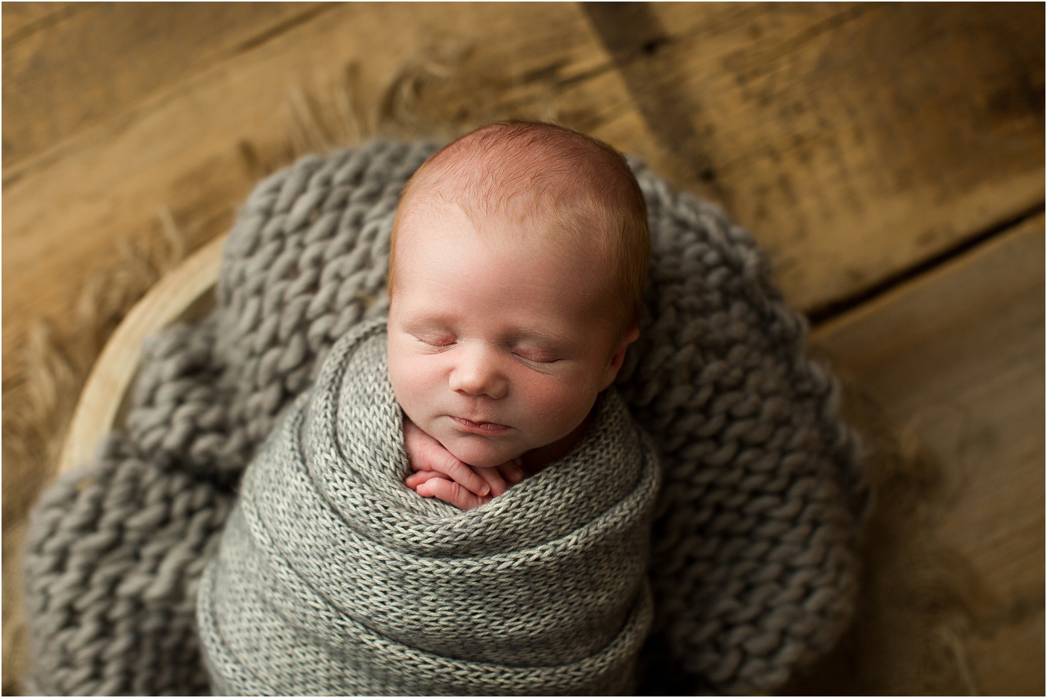 newborn boy wrapped in gray knits on barnwood