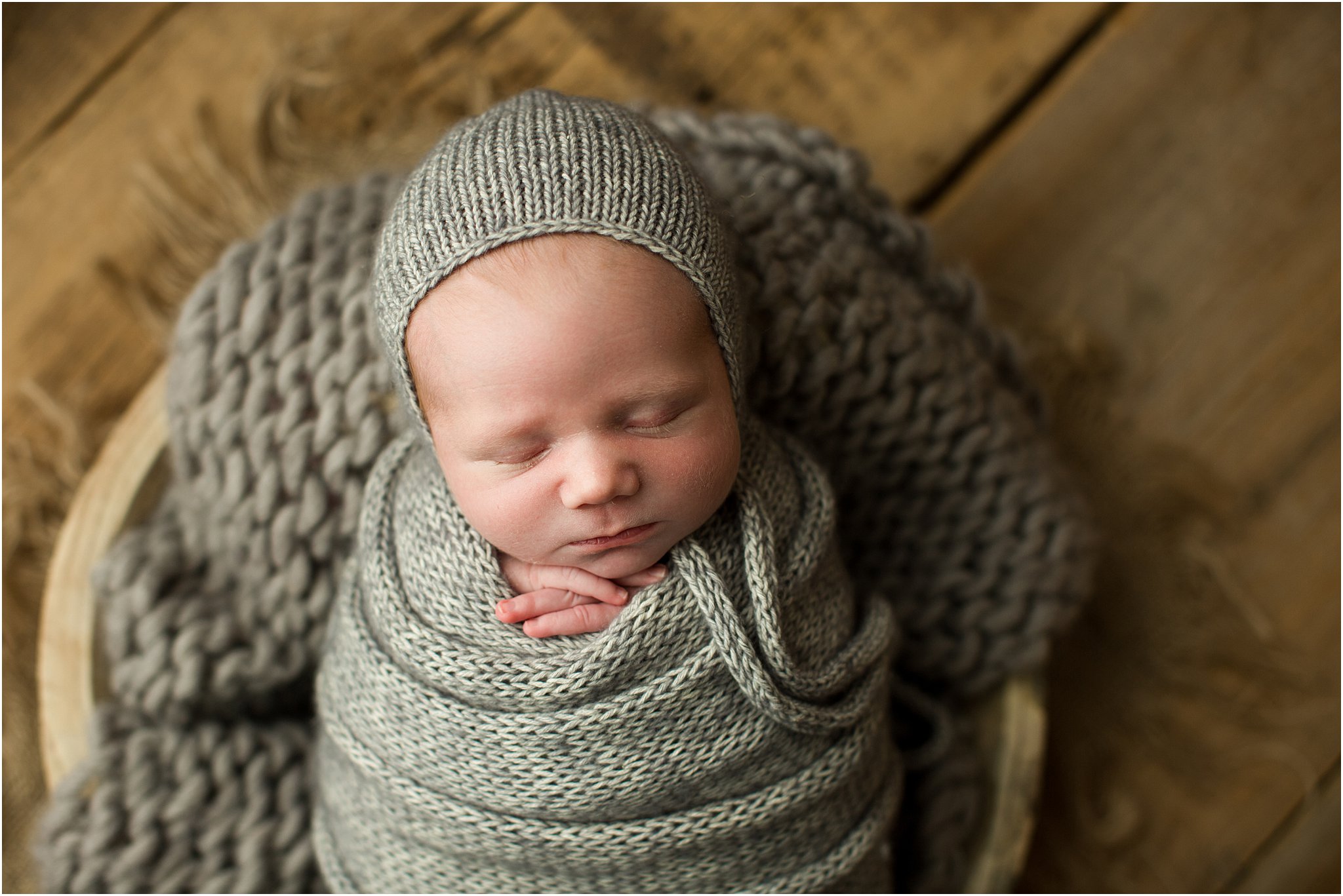newborn baby in gray knit wrap and bonnet on barnwood