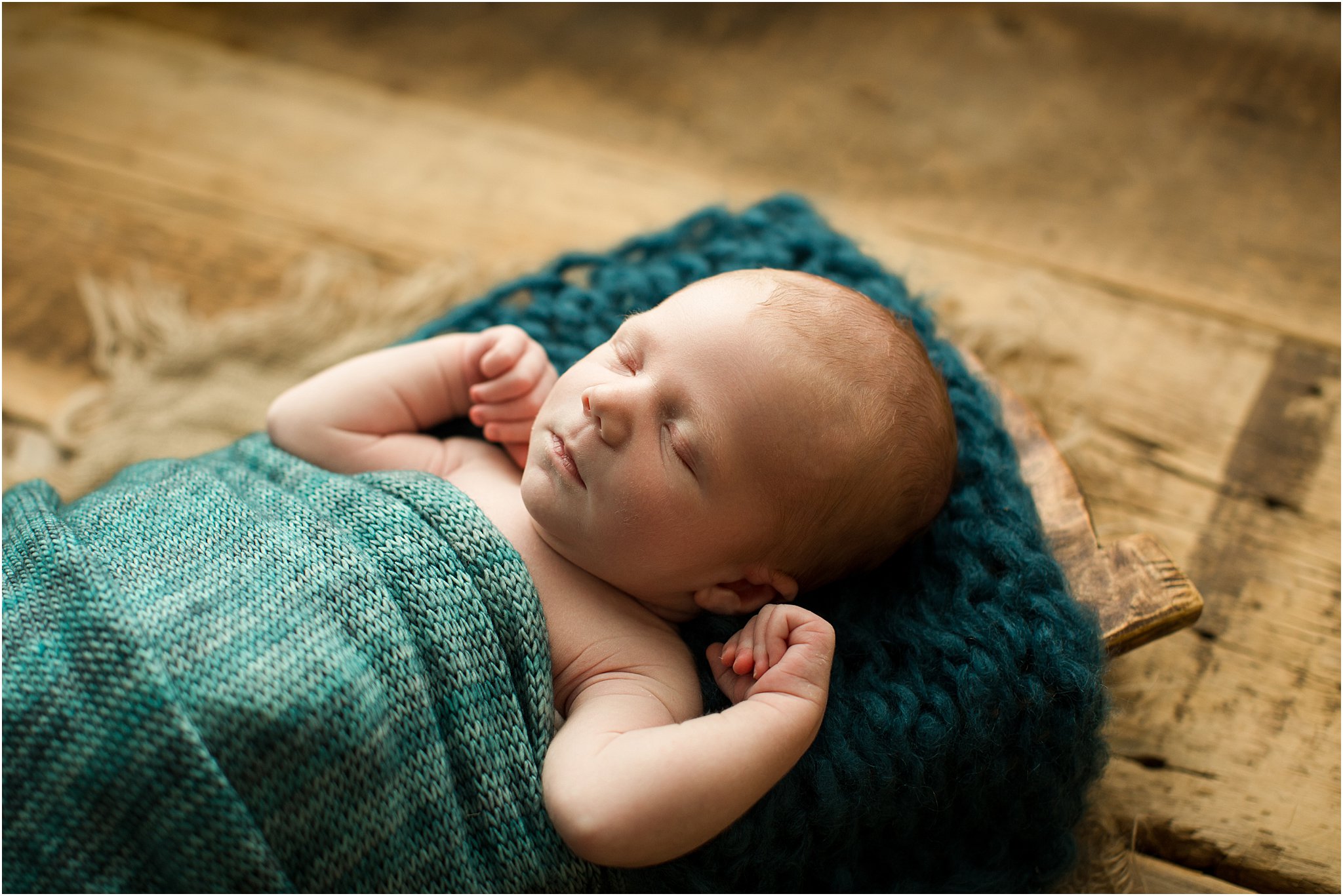 newborn wrapped in teal knits laying in wooden prop on barnwood