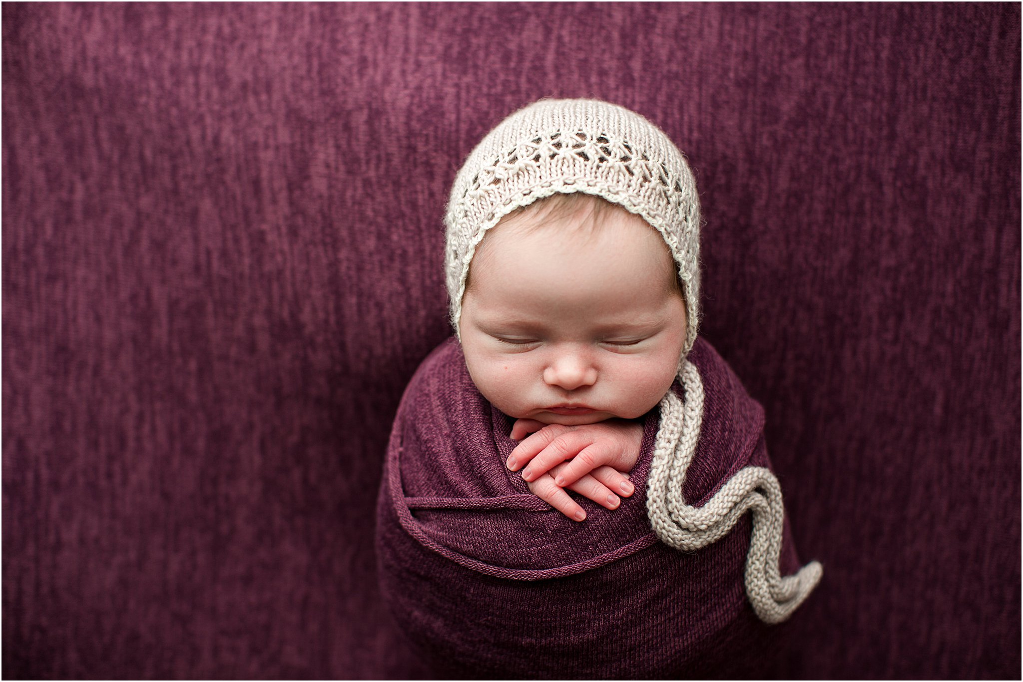 newborn girl with knit bonnet on mulberry backdrop