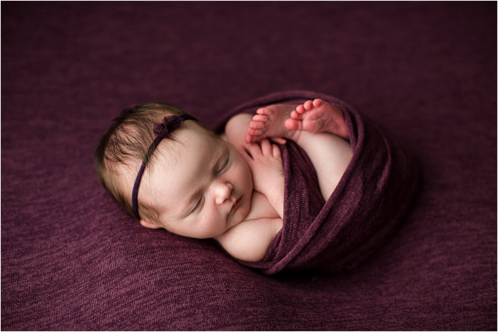 newborn baby girl wrapped in mulberry fabric