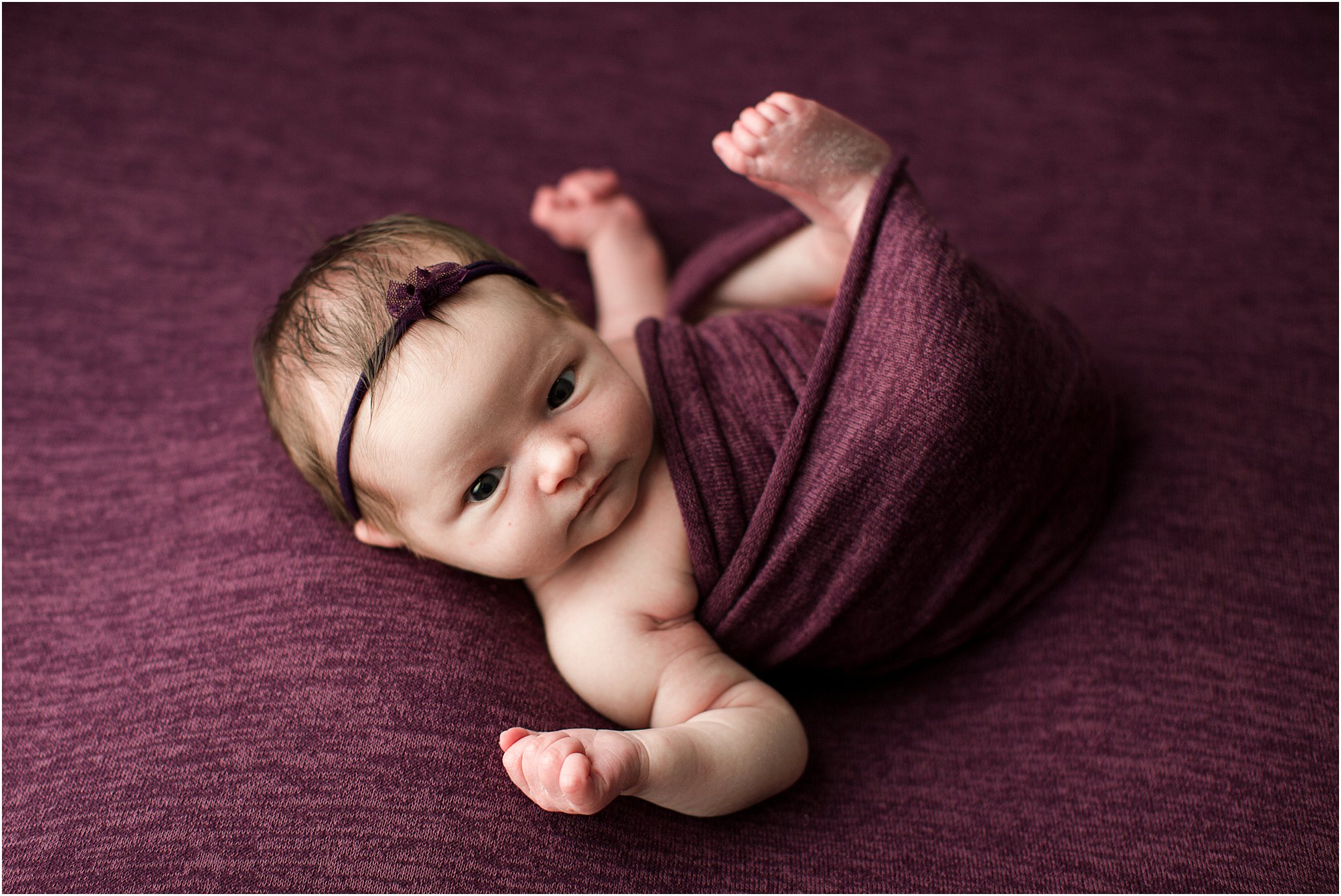 wide awake newborn baby wrapped in purple fabric