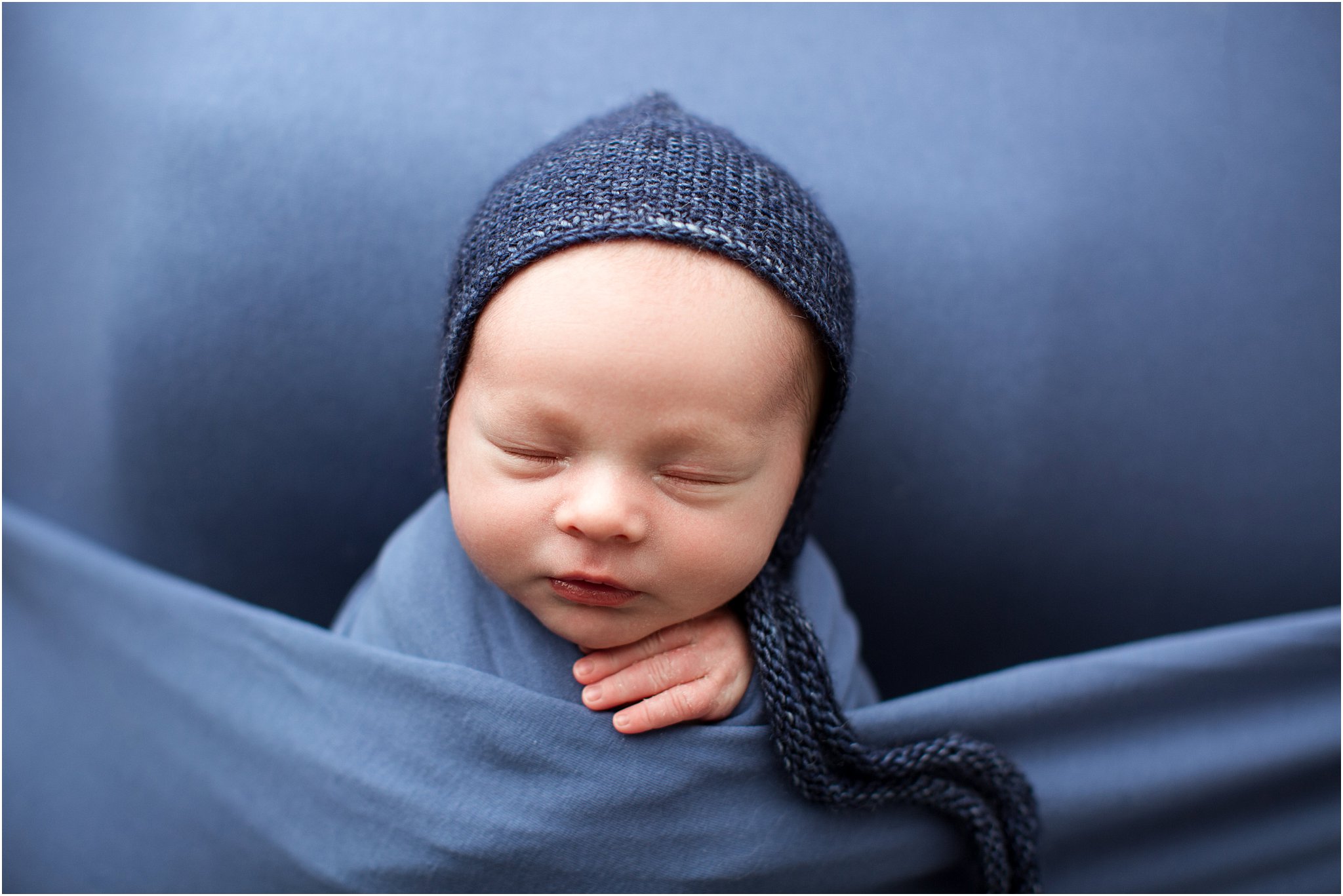 newborn boy wrapped in blue wearing a knit bonnet