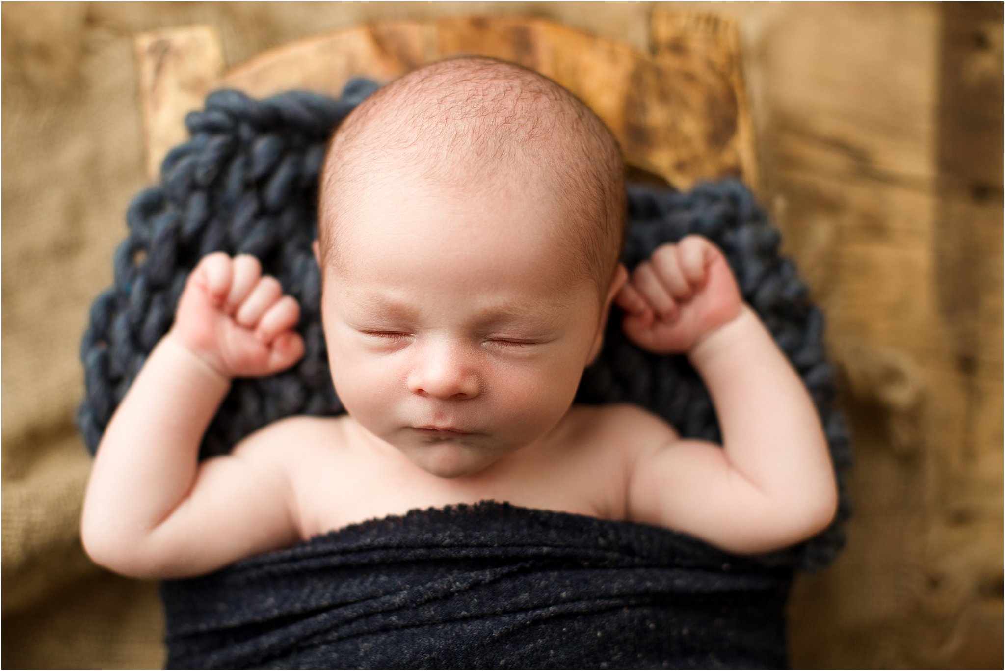 newborn boy posed with arms up on barnwood