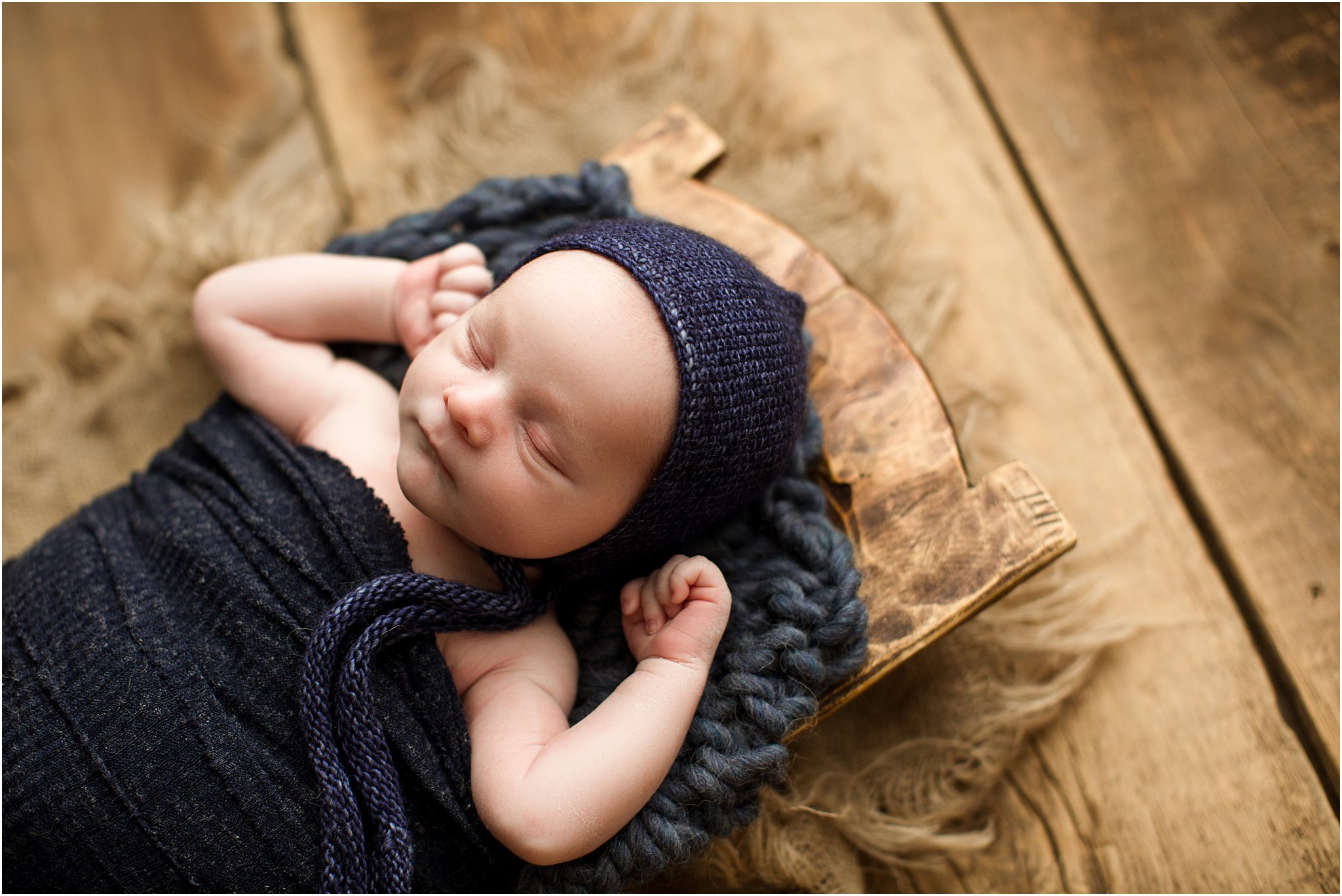 newborn boy wearing navy bonnet posed in wooden trencher