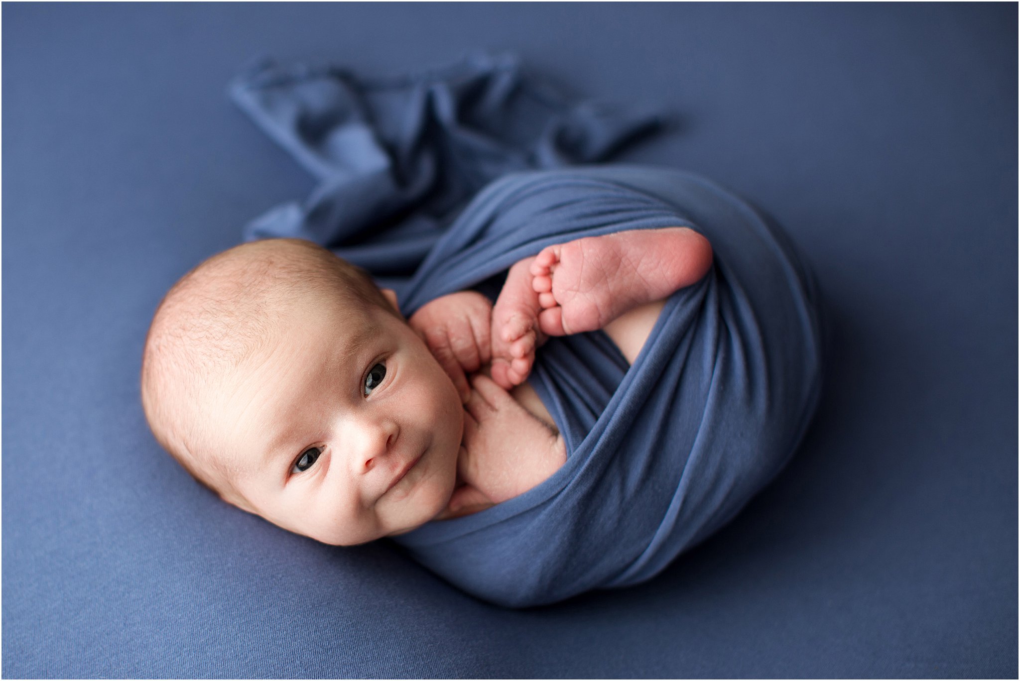 wide awake newborn boy wrapped in blue smiling