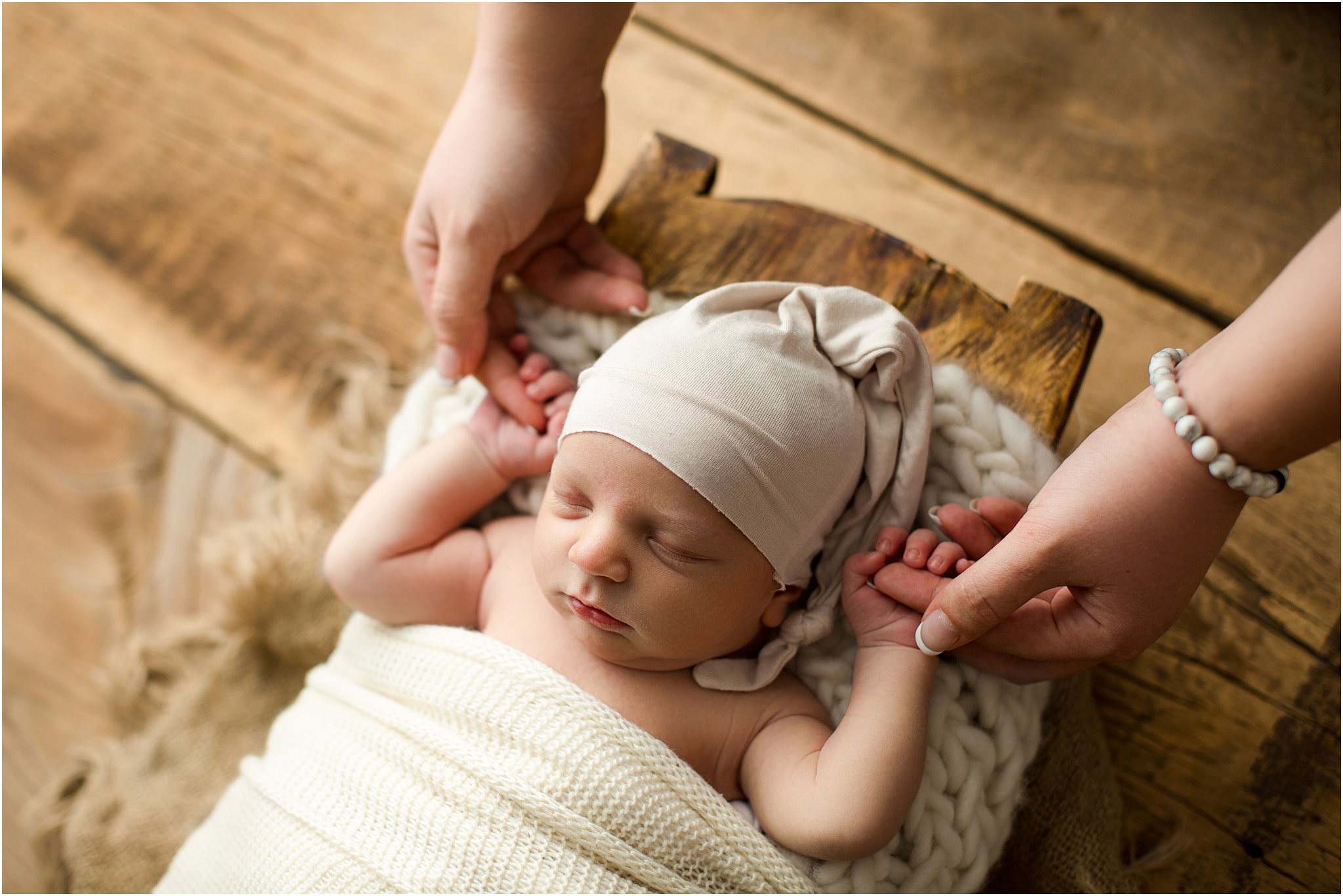 newborn boy posed on barnwood holding mom's hands