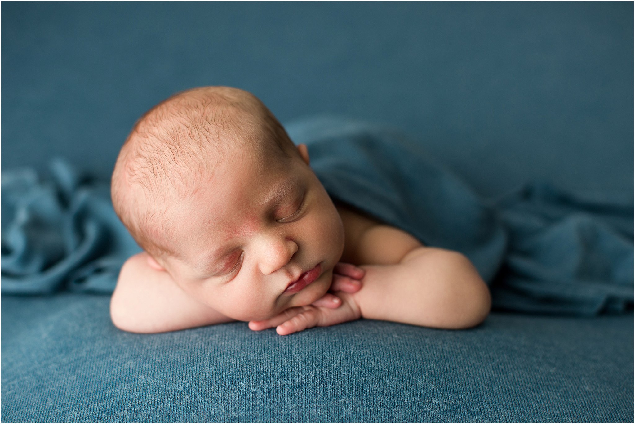 baby boy posed with hands under chin on blue blanket