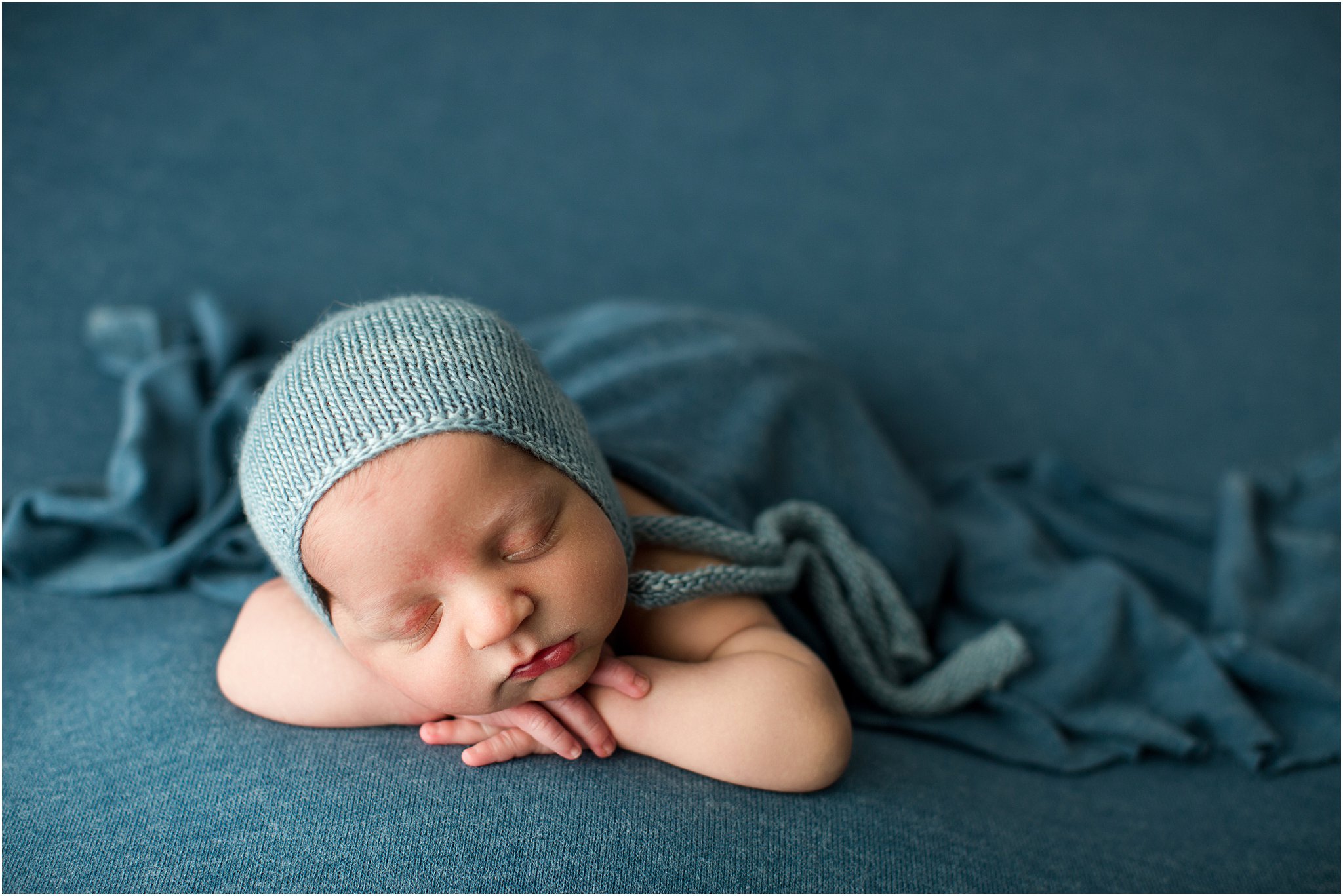 baby boy posed on blue fabric wearing a knit bonnet