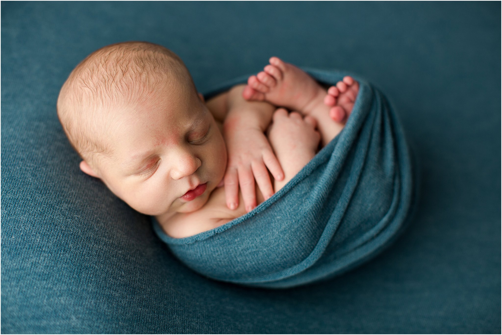 curled up newborn boy posed on blue fabric