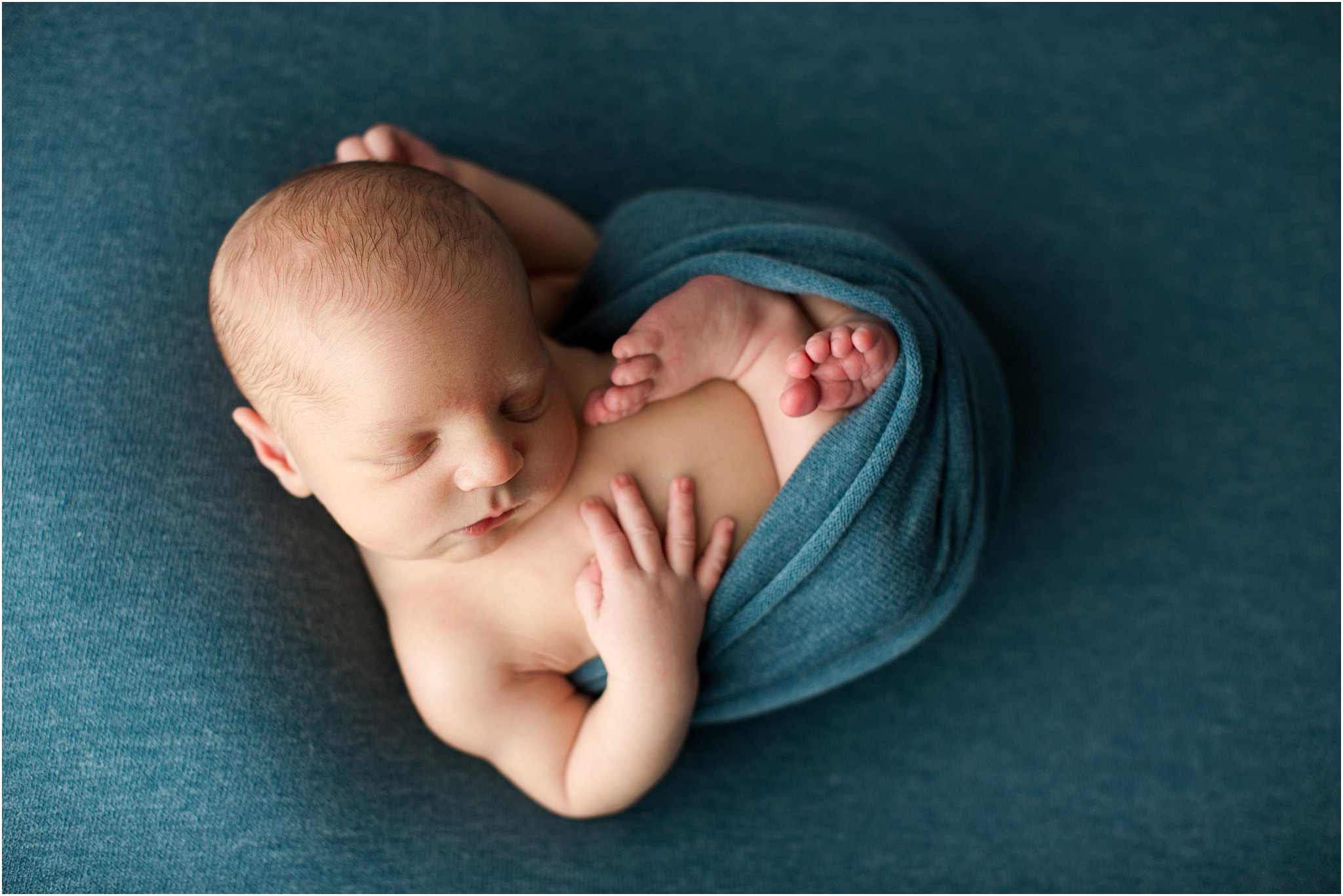 newborn in relaxed pose on blue background