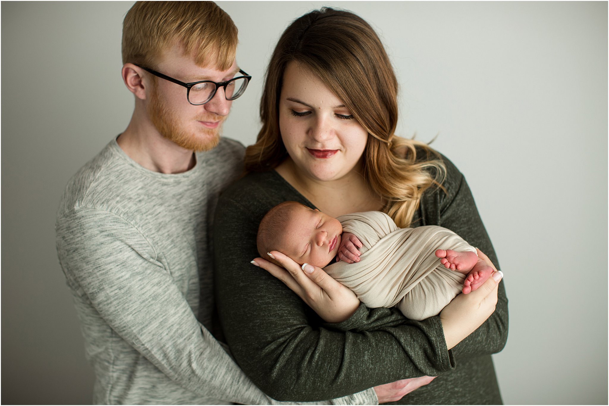 new parents holding baby boy in front of white backdrop