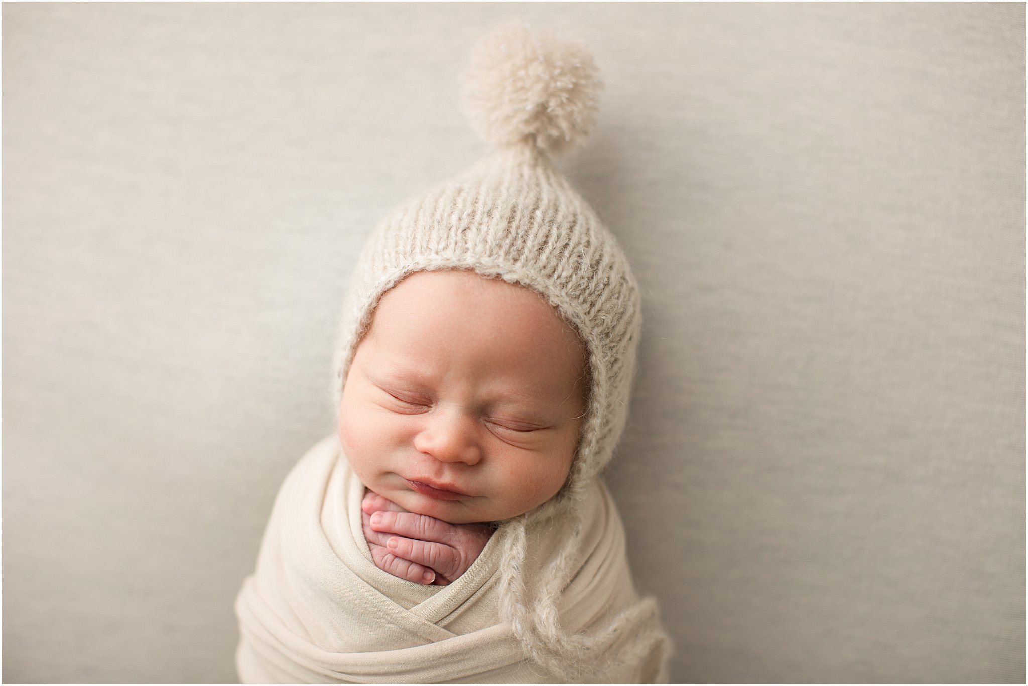 Newborn boy swaddled with pom hat