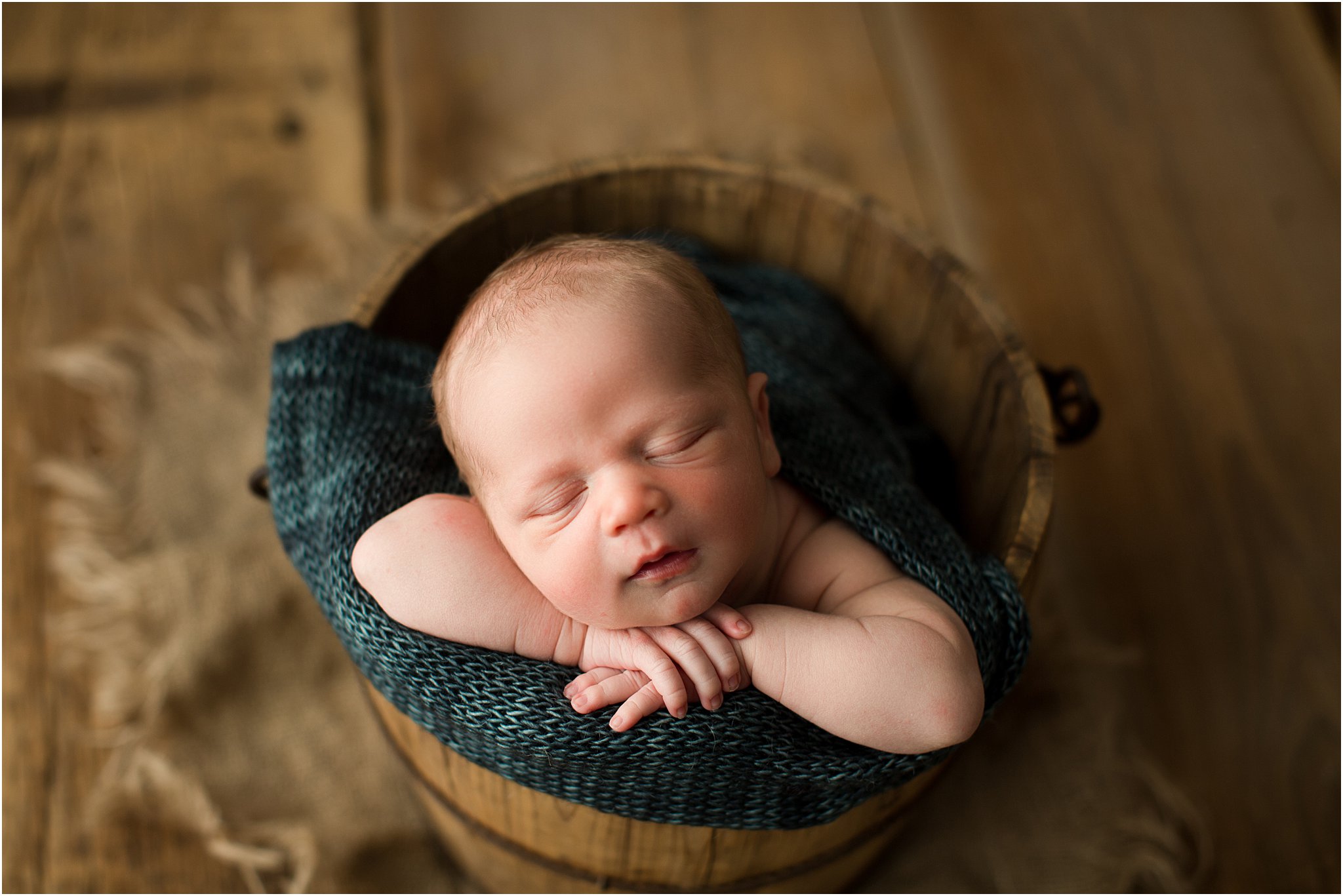newborn boy in wooden bucket on barnwood