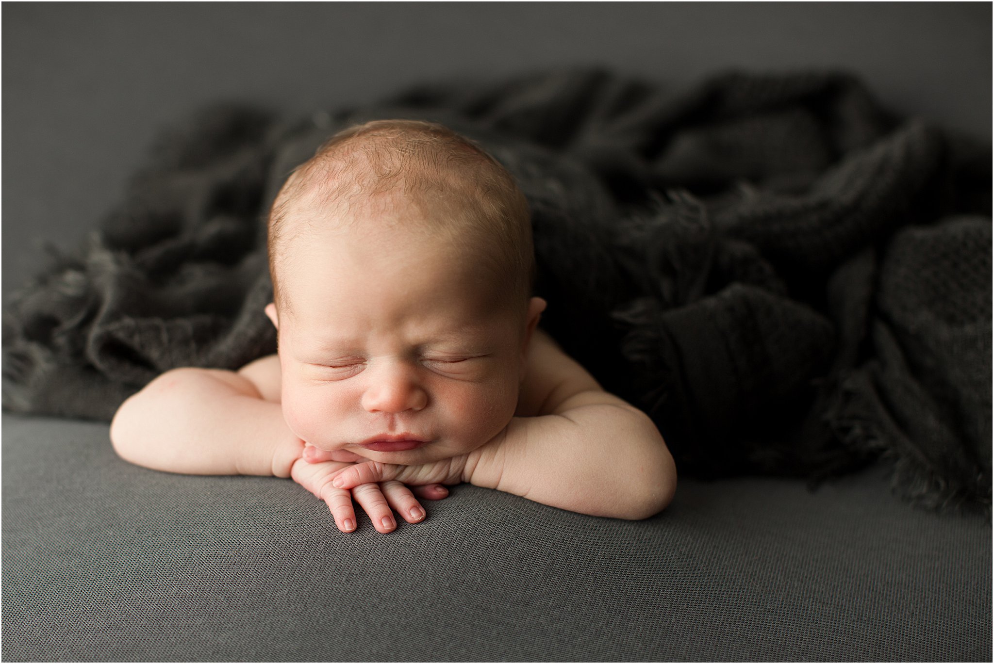 newborn boy with hands under chin