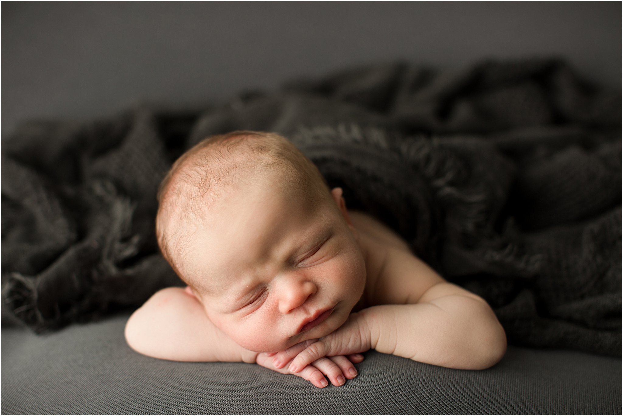 newborn boy laying on gray fabric