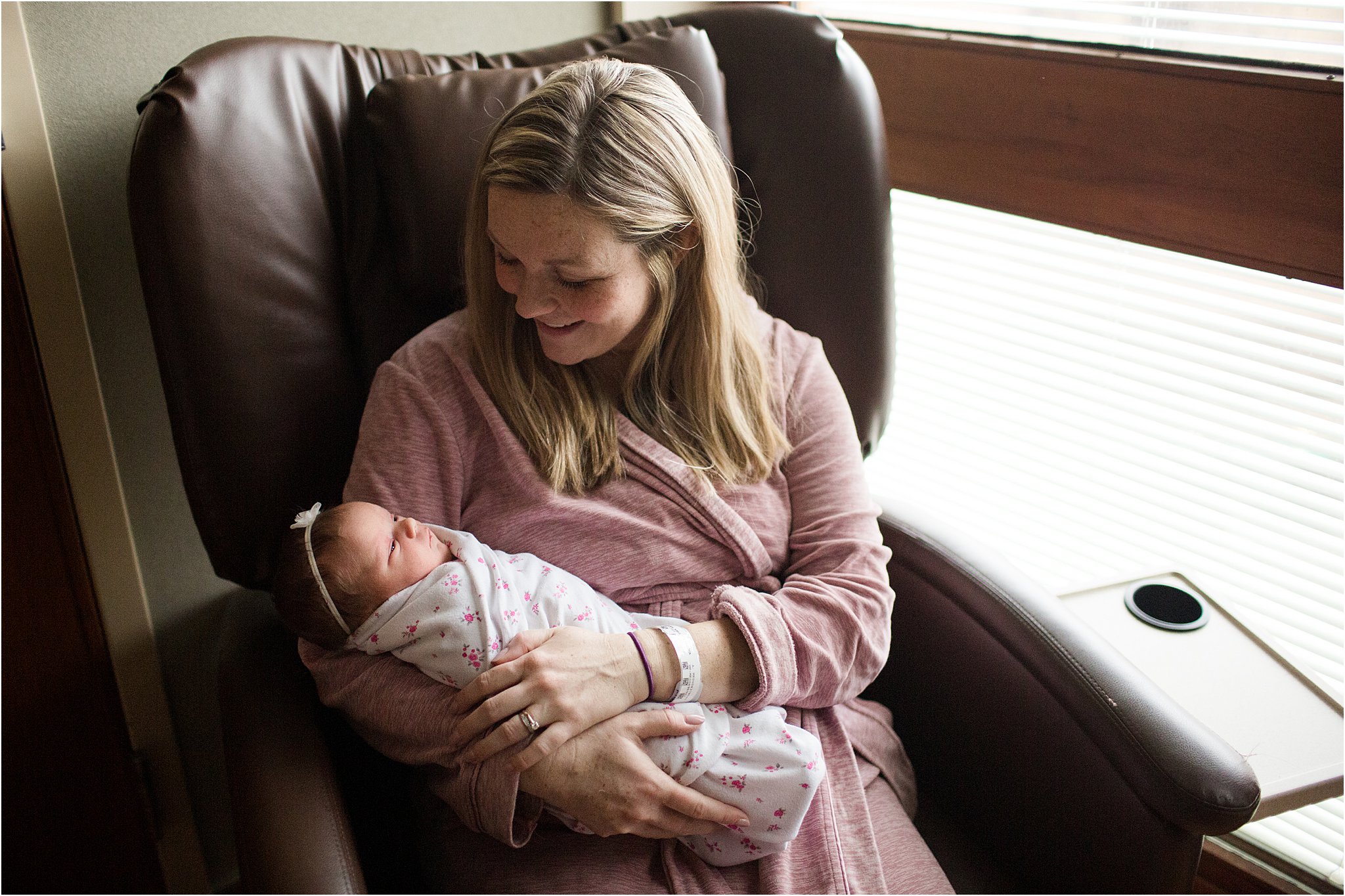 mom holding newborn baby near window in hospital