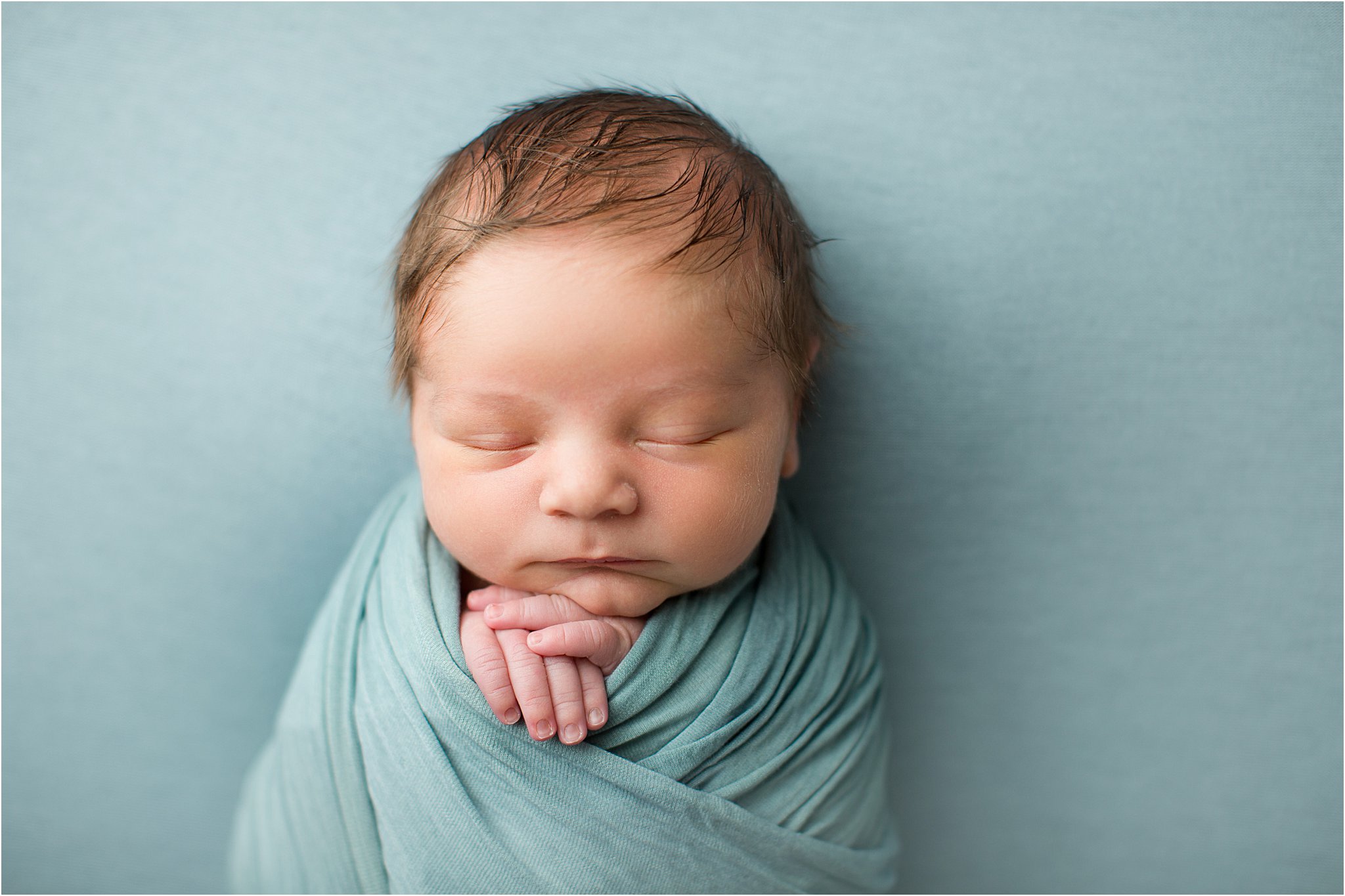baby boy with lots of hair swaddled on blue backdrop