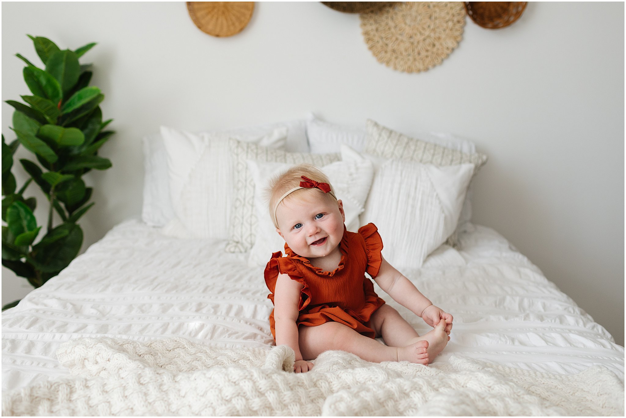 baby girl on bed in rust romper smiling